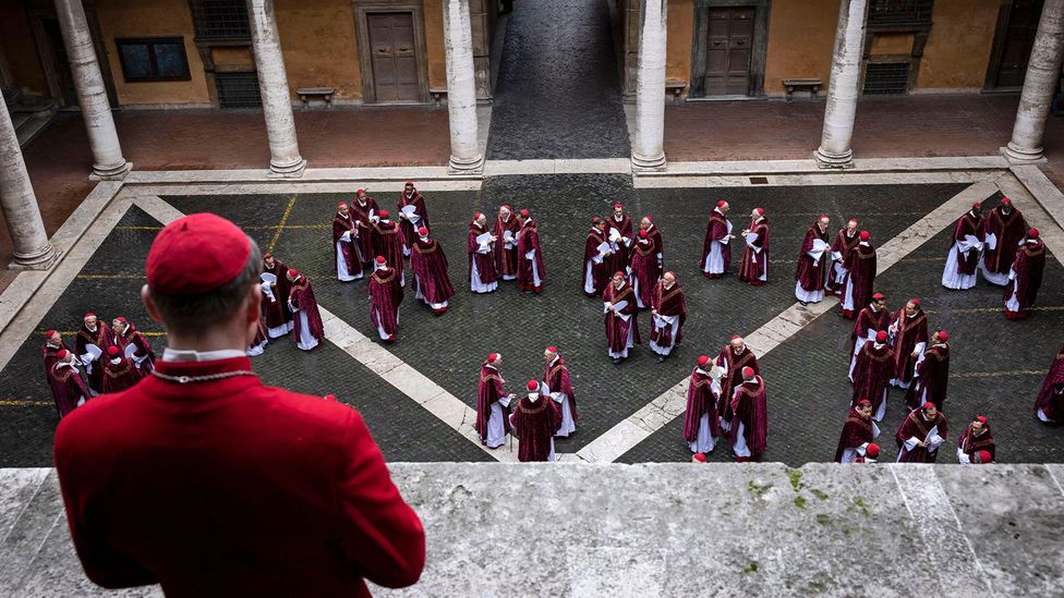 A Catholic cardinal looks down at a courtyard with many groups of cardinals in a scene from Conclave (Credit: Alamy)