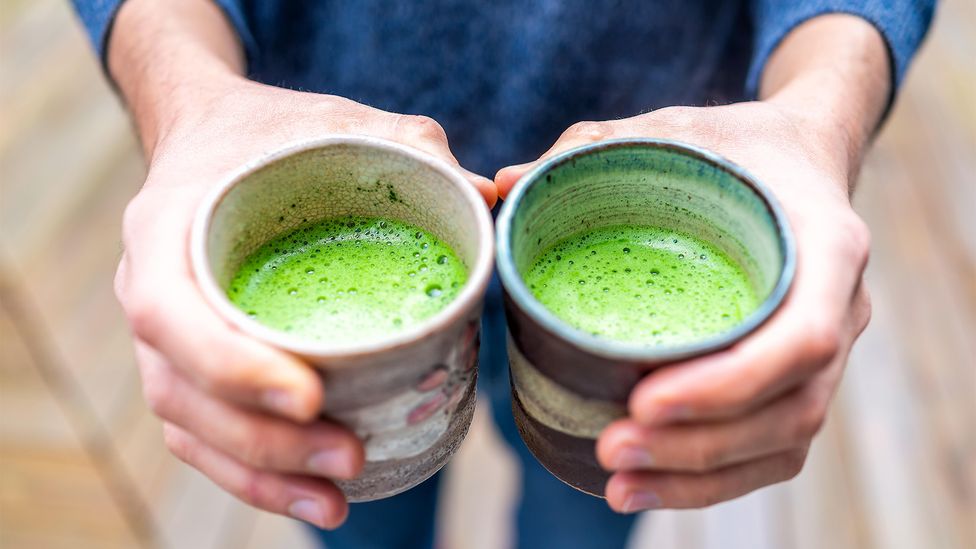 Closeup of hands holding two cups of green matcha (Credit: Alamy)