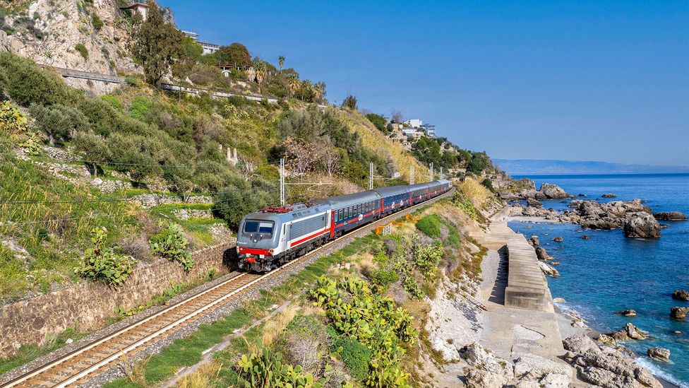 Silver and red train on track next to the sea in Sicily (Credit: Alamy)