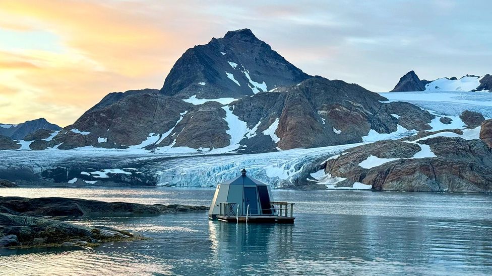 Smal modern cabin floating on calm water with snow-dusted mountains in background (Credit: Floating Glacier Hut) Smal modern cabin floating on calm water with snow-dusted mountains in background (Credit: Floating Glacier Hut)