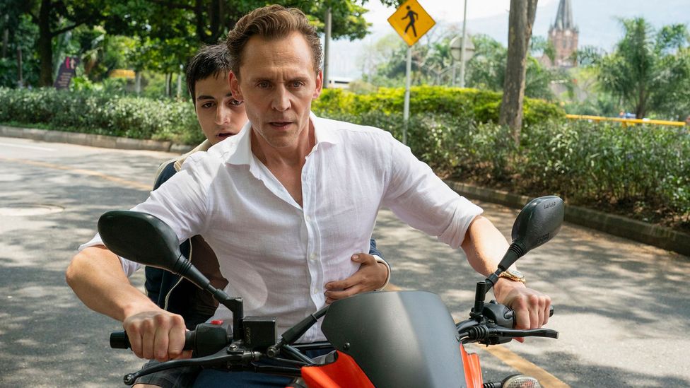 Tom Hiddleston riding a motorcycle with a young boy sat behind him in The Night Manager season two (Credit: BBC)