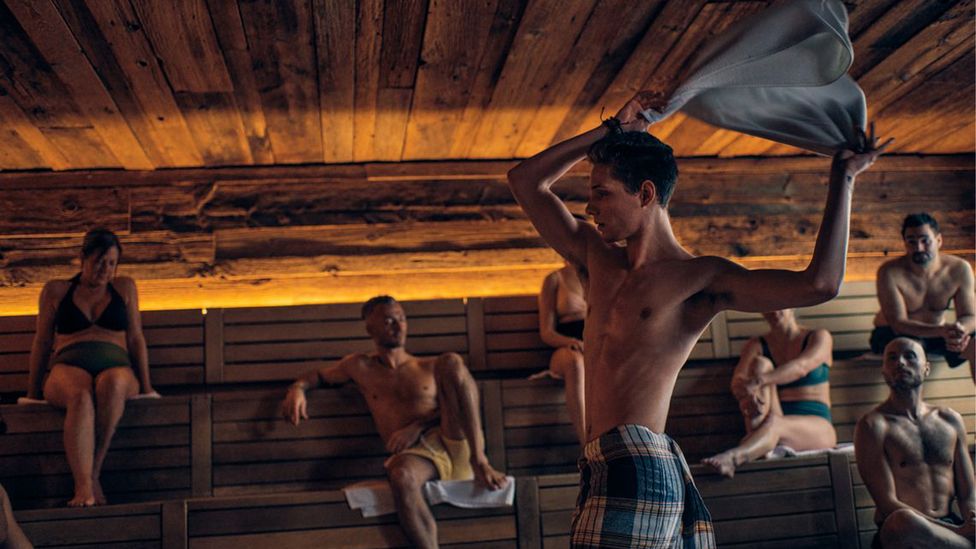 An Aufgussmeister twirls a towel in a sauna as a crowd watches around him (Credit: Getty Images)