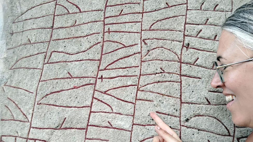 A woman looking and pointing at some runes on a stone (Credit: Magnus Källström, the Swedish National Heritage Board)