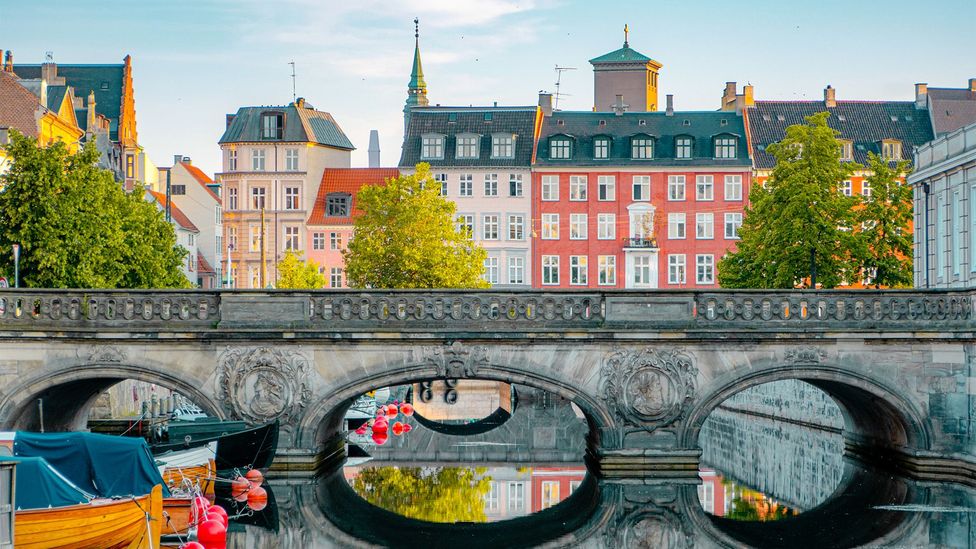 Historic stone bridge over a canal with colourful townhouses and trees along the waterfront in Copenhagen (Credit: Getty Images)