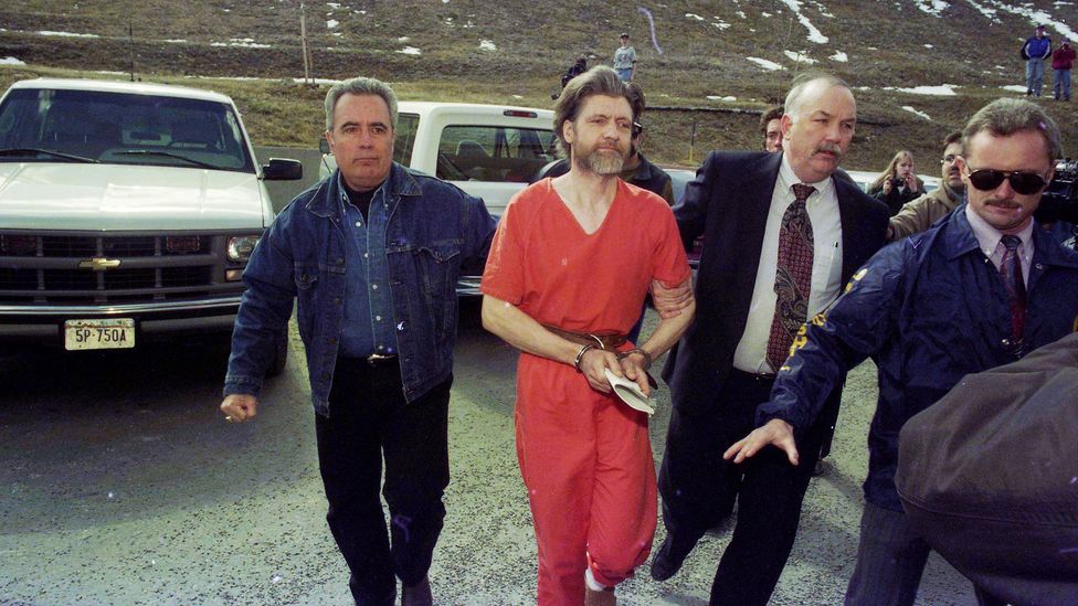 Theodore Kaczynski, the Unabomber, dressed in an orange prison jumpsuit and handcuffed, being led by federal agents (Credit: Getty Images)