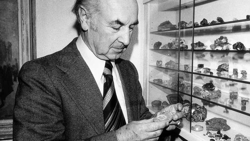 Black-and-white photo of Albert Hofmann in a suit and tie examining a collection of rocks on a shelf in 1976 (Credit: Getty Images)