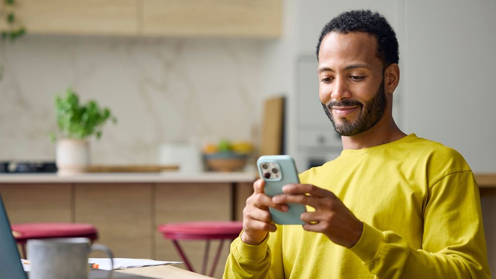 A man sits staring at his phone and smiles at it (Credit: Getty Images)