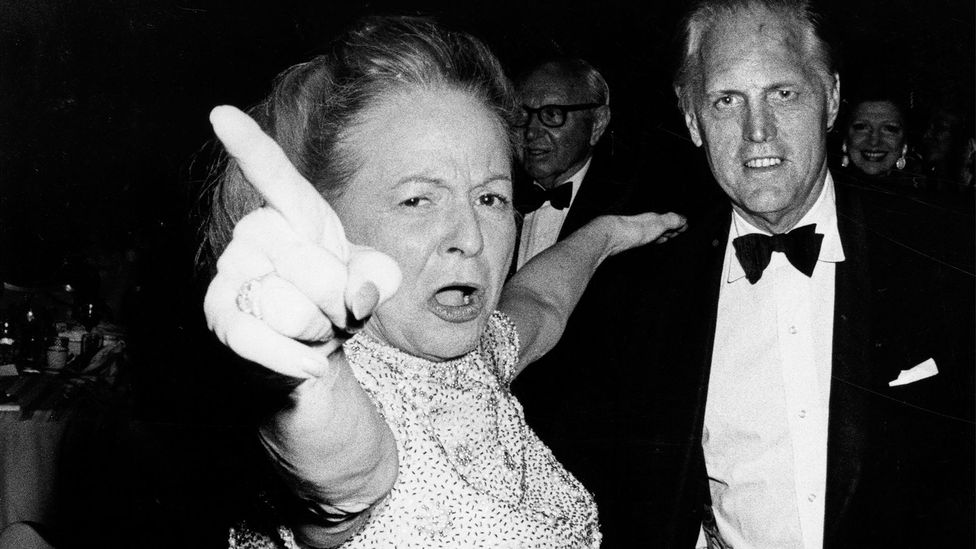 Black and white photograph of Martha Mitchell pointing her finger to the sky with her arm around a man wearing a tux (Credit: Getty Images)