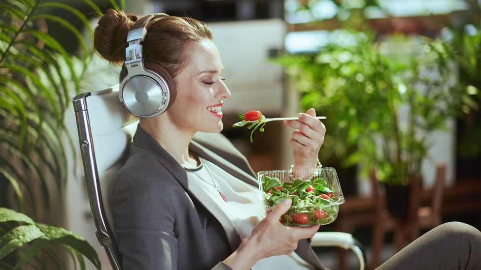 Woman wearing headphones eats a salad (Credit: Getty Images)