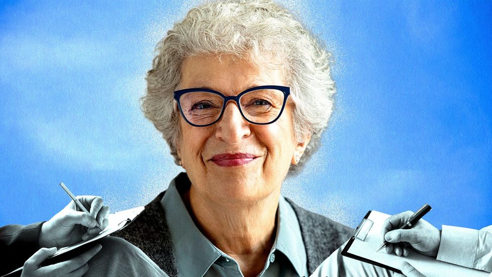 An older woman with white hair and glasses smiles, while the hands of therapists writing notes surround her (Credit: Serenity Strull/ BBC/ Getty Images)