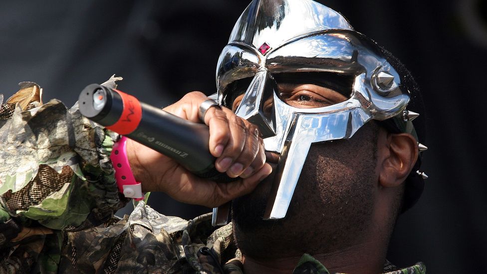 MF Doom rapping into a microphone and wearing a mask (Credit: Getty Images)
