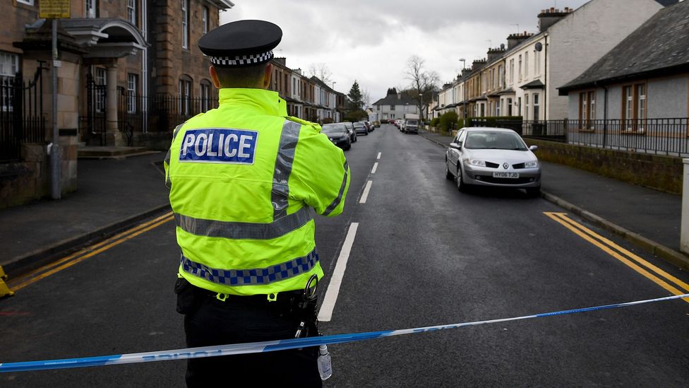 A police officer in a high-visibility jacket standing behind blue and white police tape closing off a residential street in Glasgow (Credit: Getty Images)
