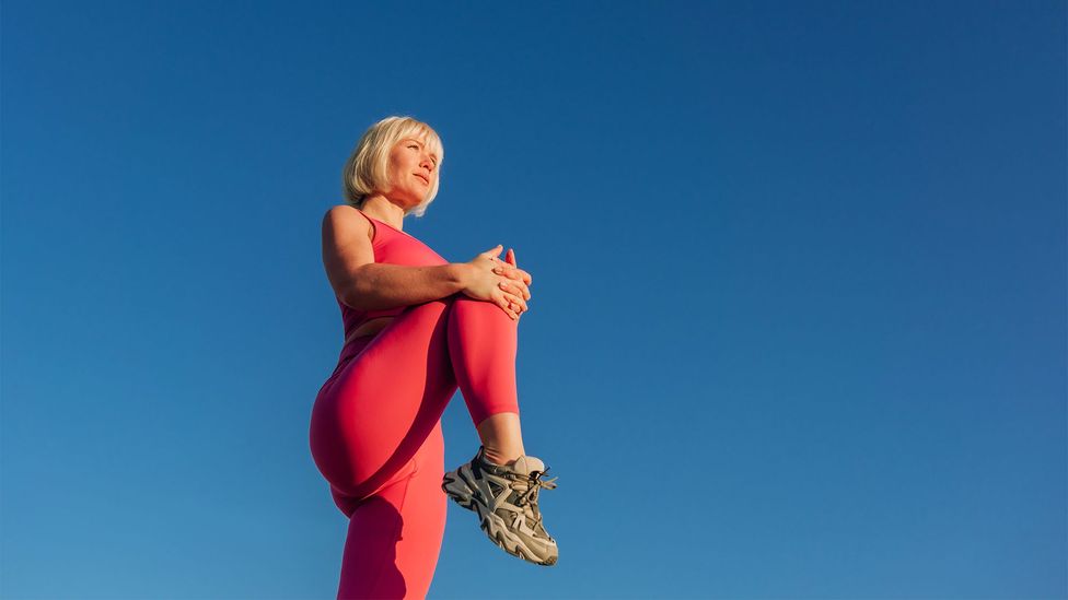 A woman in pink sportswear stretches, against a deep blue sky (Credit: Getty Images)
