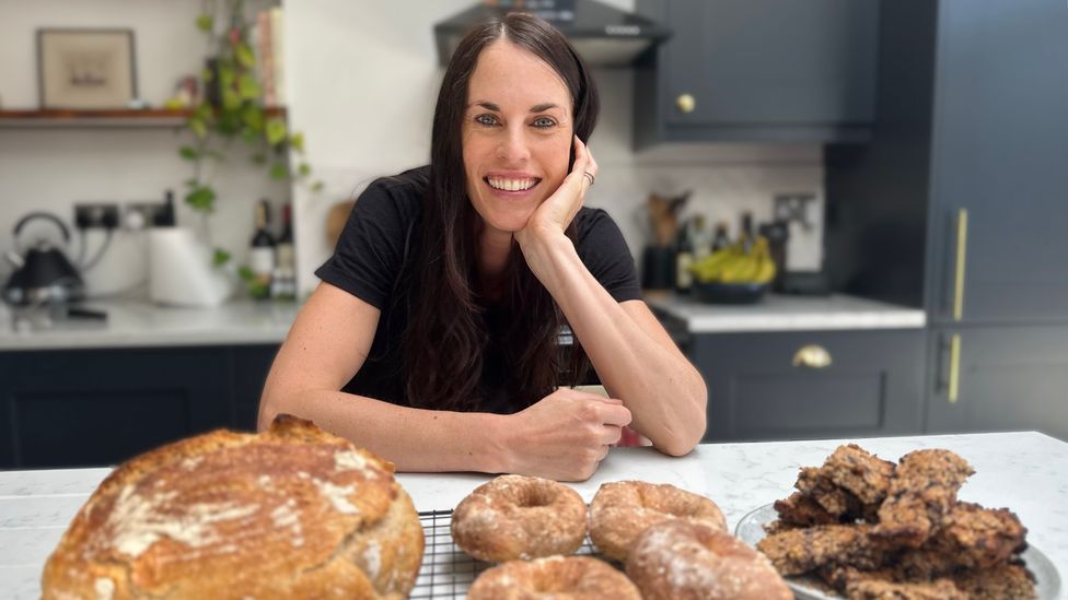 Melissa Hogenboom poses with homemade bread, bagels and oat bars on a kitchen counter (Credit: Stephen Parker)
