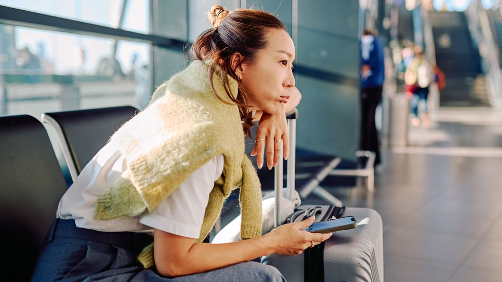 Woman sitting with her luggage in an airport terminal (Credit: Getty Images)