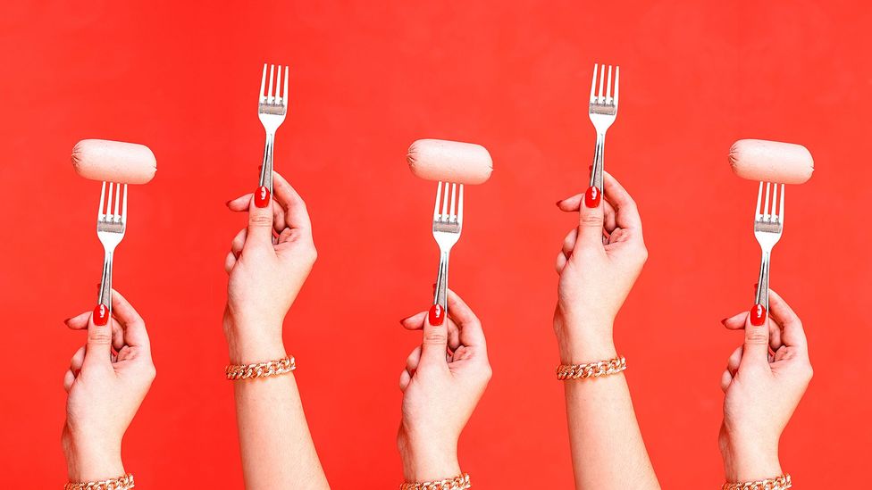Five hands raise forks to the air, three of them have sausages on them (Credit: BBC/ Javier Hirschfeld/ Getty Images)