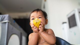 A baby with broccoli pieces in front of them (Credit: Getty Images)